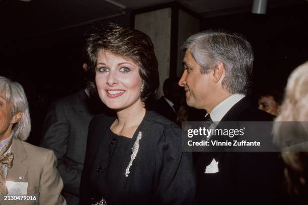 American actress and fashion model Cristina Ferrare, wearing a black outfit with a lizard brooch, and her husband, American film executive Anthony...