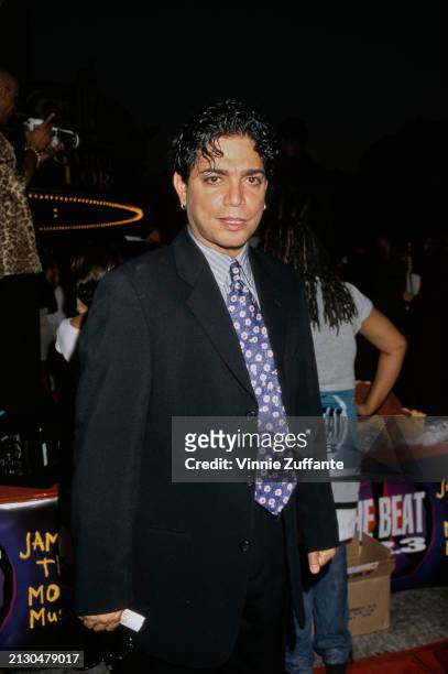 American actor and dancer Michael DeLorenzo, wearing a black suit over a white-and-blue striped shirt and a blue tie with floral motifs, attends the...