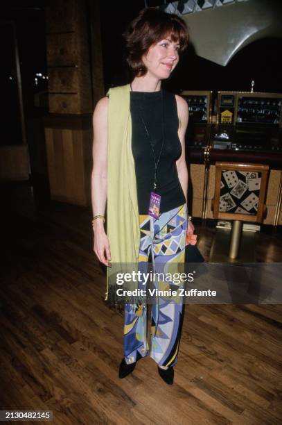 American actress Dana Delaney, wearing a black sleeveless top and trousers with a blue, yellow and white geometric pattern, with a pale green scarf,...