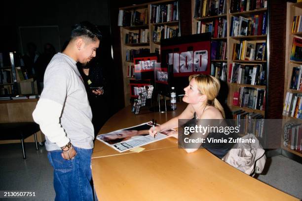 British singer and songwriter Dido, wearing a black v-neck haltertop, sits behind a table and signs a poster for a fan during an in-store promotion...