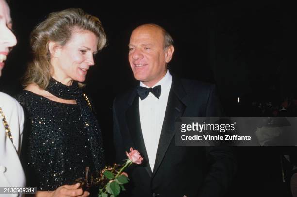 American actress Candice Bergen, wearing a black sequin evening gown with matching scarf, and American businessman Barry Diller, who wears a tuxedo...
