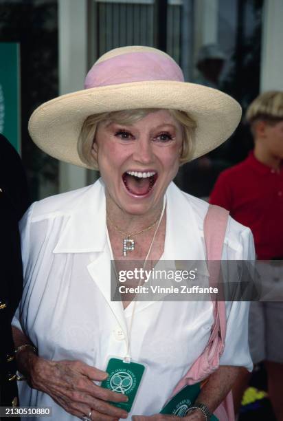 American comedian and actress Phyllis Diller, wearing a straw hat with a pink hatband, a white outfit and a necklace with a 'P' pendant, attends the...