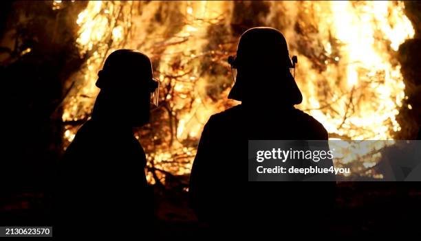 feuerwehrleute mit feuer im hintergrund - feuerwehr deutschland stock-fotos und bilder