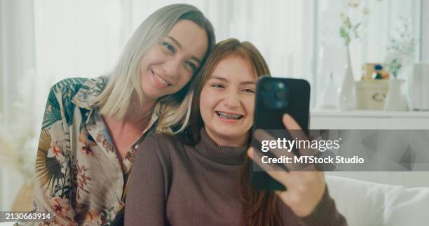 happy family young mom and daughter use phone video call online to friends spend time sitting on sofa in living room at home. family happy moment. - friends laughing at iphone video stock pictures, royalty-free photos & images