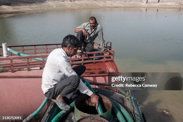 Tanker drivers Mankaran Bishnoi and Hermana Bishnoi collect water to be delivered to villages from a rain-fed pond on March 31, 2024 near Samlani...