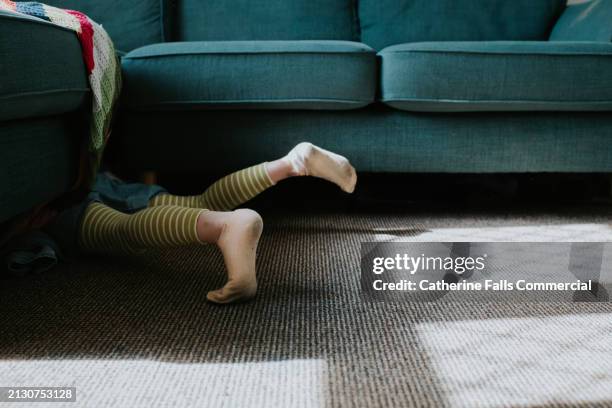 a little girl, wearing dirty socks, crawls under a sofa - female twins stock pictures, royalty-free photos & images