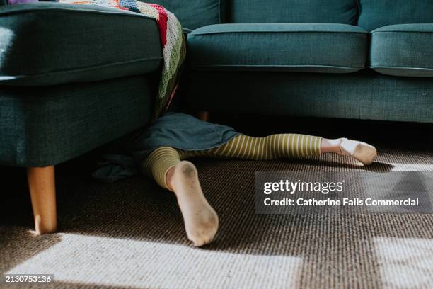 a little girl, wearing dirty socks, crawls under a sofa - smelly laundry stock pictures, royalty-free photos & images