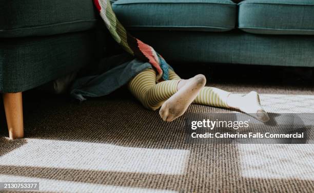 a little girl, wearing dirty socks, crawls under a sofa - kids mess carpet stock pictures, royalty-free photos & images