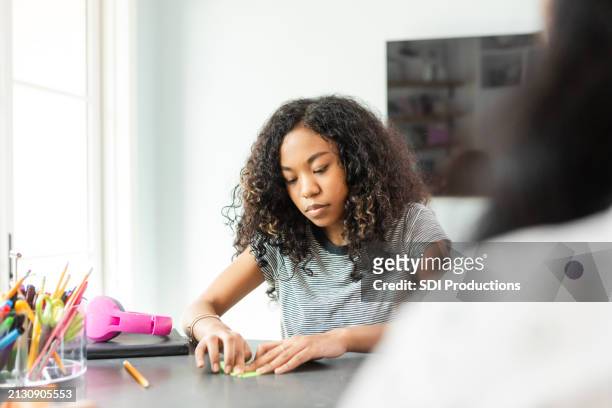 young female high school student carefully folds paper while working on arts and crafts - origami instructions stock pictures, royalty-free photos & images