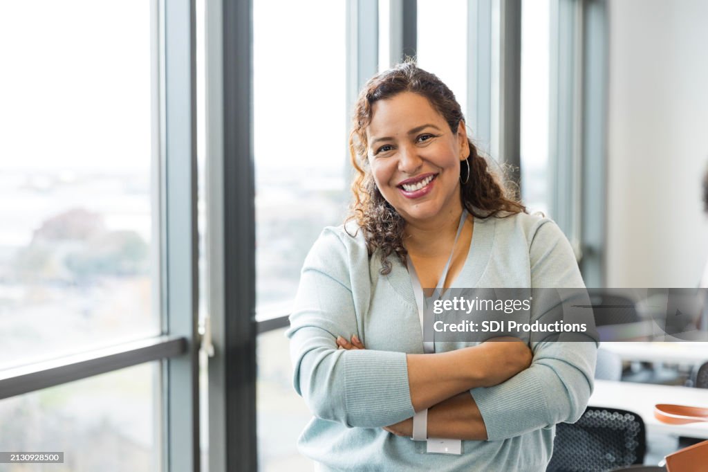 Cheerful female teacher stands with arms crossed in classroom