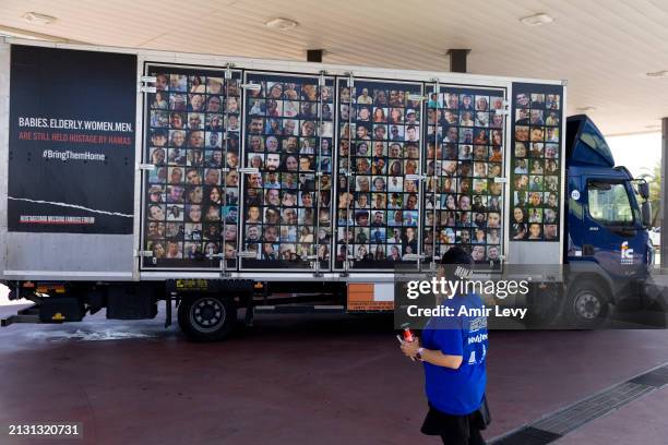 Woman looks at a truck covered with photos of hostages held in the Gaza Strip as it is standing in a gas station on April 4, 2024 in Kfar Aza,...