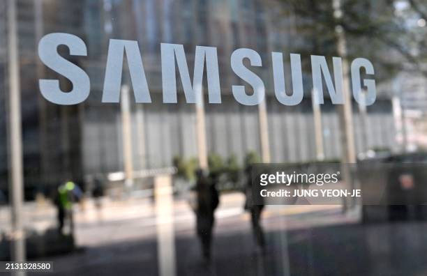 People walk past the Samsung logo displayed on a glass door at the company's Seocho building in Seoul on April 5, 2024. Samsung Electronics said on...