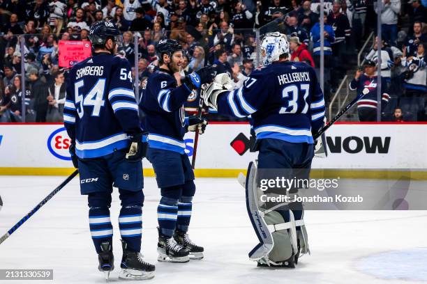 Goaltender Connor Hellebuyck of the Winnipeg Jets celebrates with teammates Dylan Samberg and Colin Miller following a 5-2 victory over the Calgary...