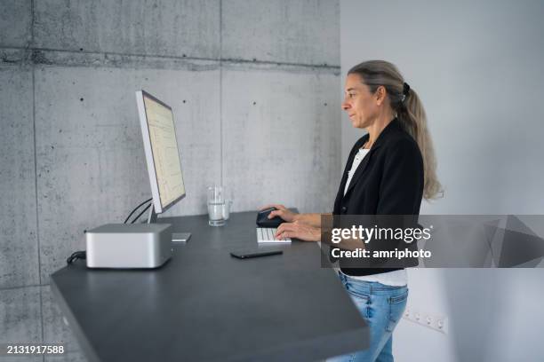 woman working at adjustable stand computer desk in home office - ergonomie stockfoto's en -beelden