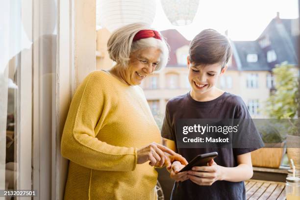 smiling senior woman using smart phone held by grandson standing in balcony - balkon berlin stock-fotos und bilder