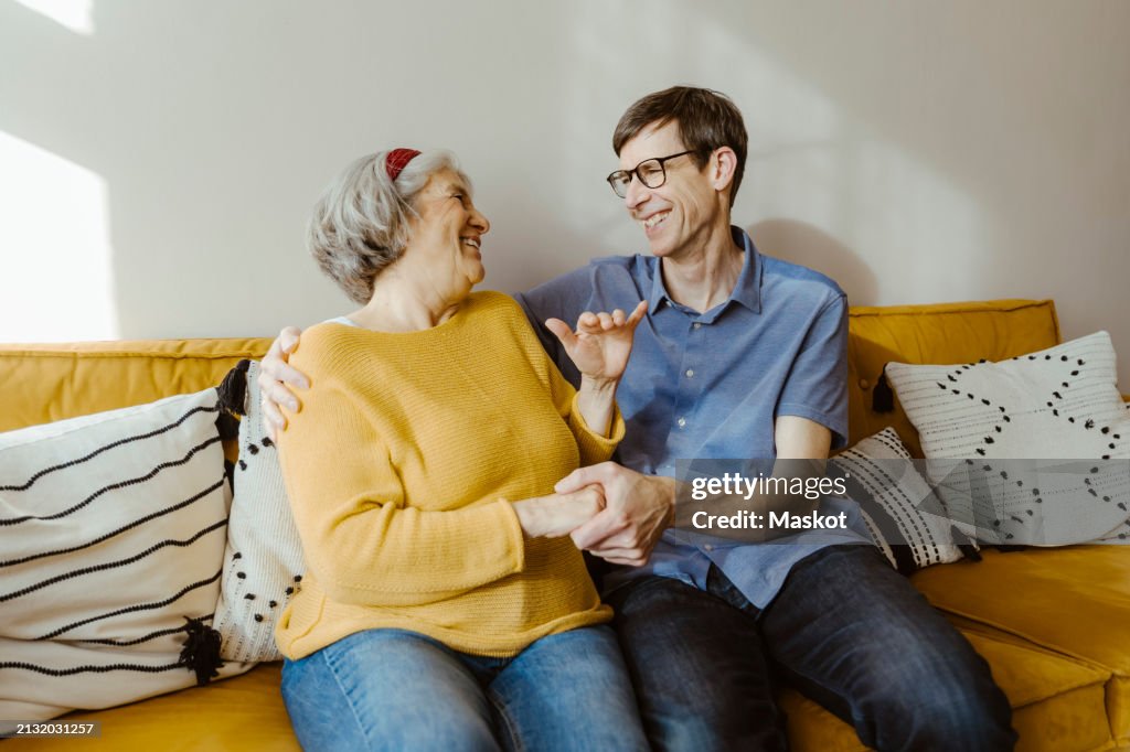 Happy man with arm around senior mother-in-law sitting on sofa at home