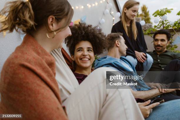 smiling woman talking with female friends while sitting at party in balcony - rooftop deck stock pictures, royalty-free photos & images