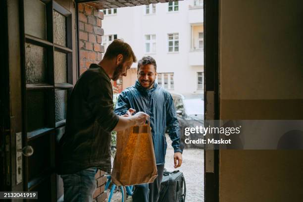 side view of man receiving parcel from delivery person while standing at doorway - delivering stock pictures, royalty-free photos & images