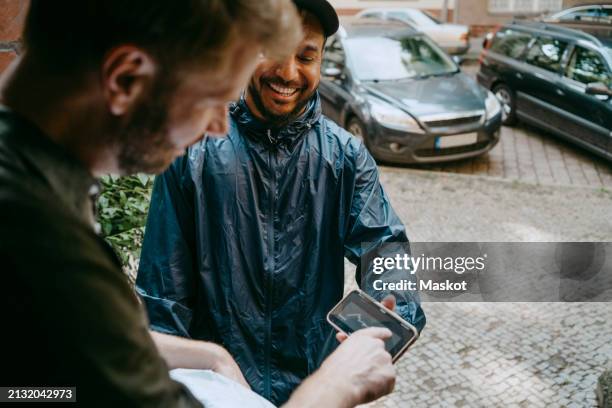 high angle view of smiling delivery person taking electronic signature from man at doorstep - firma digital fotografías e imágenes de stock