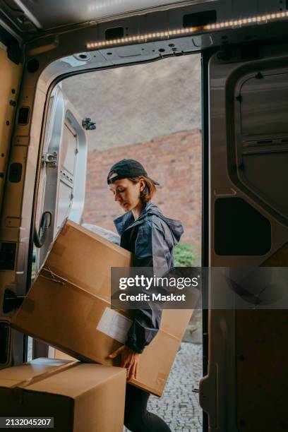 side view of female delivery person unloading box from van trunk - livreur photos et images de collection