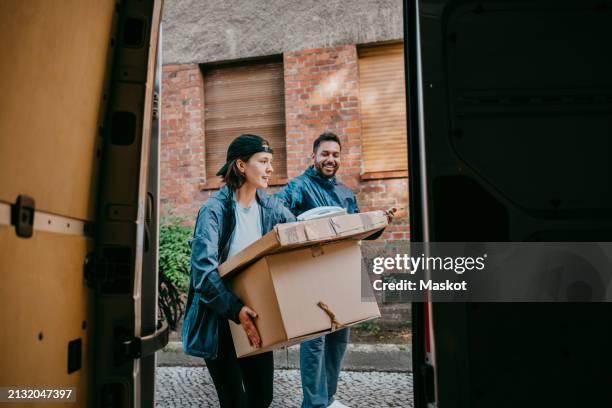 male and female delivery coworkers carrying boxes seen from van trunk - offloading stock pictures, royalty-free photos & images