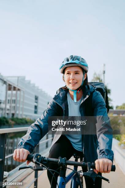 smiling female delivery person wearing helmet and sitting on bicycle - verkehrsweg für fußgänger stock-fotos und bilder