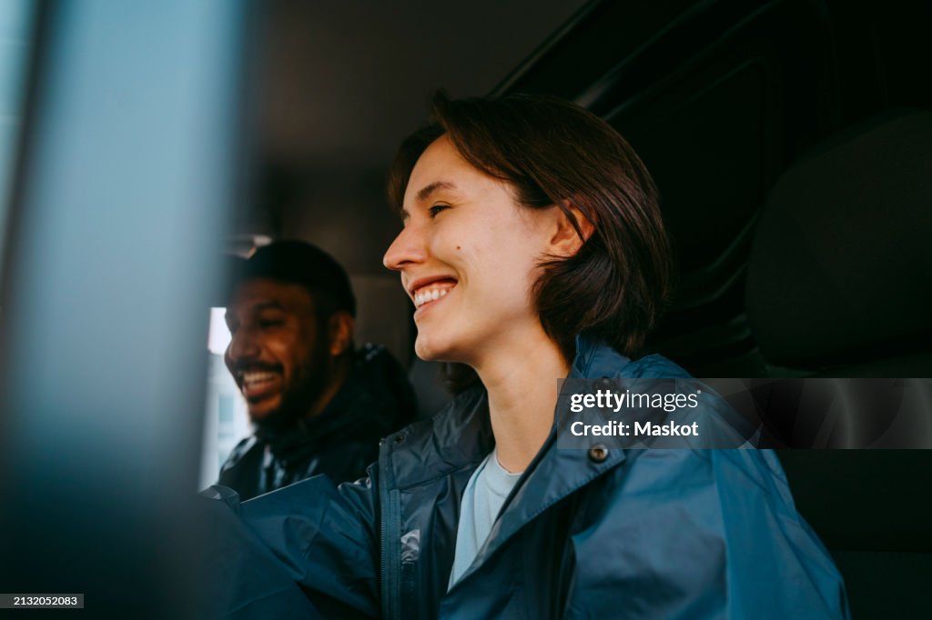 Happy female delivery person driving van while sitting with colleague