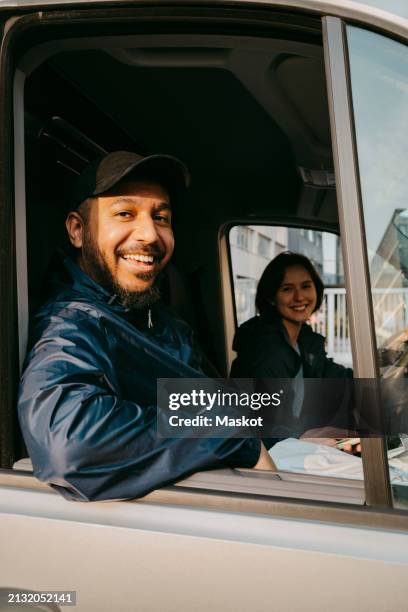 portrait of smiling male delivery person sitting with female colleague in van - livreur photos et images de collection