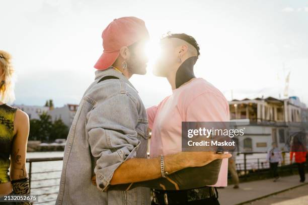 side view of romantic gay man kissing non-binary friend on promenade - beso en la boca fotografías e imágenes de stock