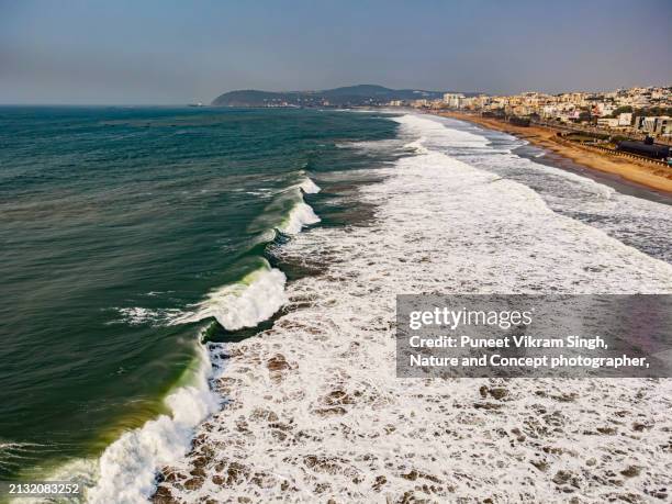 aerial view of vizag city looking towards the ramakrishna or rk beach along with the dangerous waves hitting the rocks. the famous dolphin nose can also be seen towards top end of the image. - travel destination not business travel or cityscape or scenic or exploration or vacation stockfoto's en -beelden