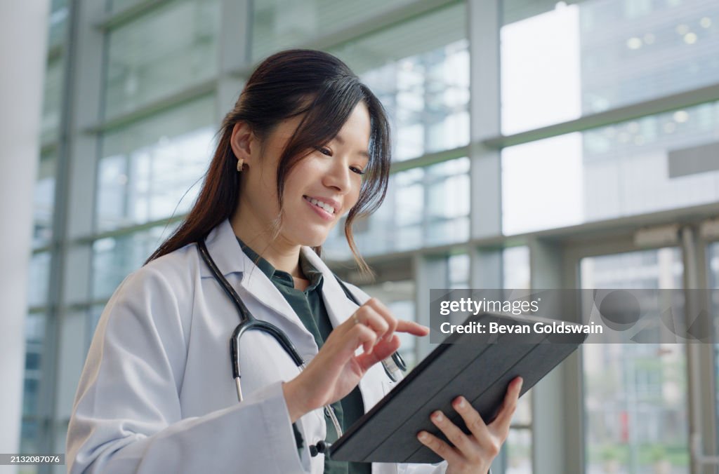 Asian woman, doctor and happy in hospital with tablet for prescriptions, research and results. Female person, digital and smile for healthcare with appointment, work and wellness in medical career