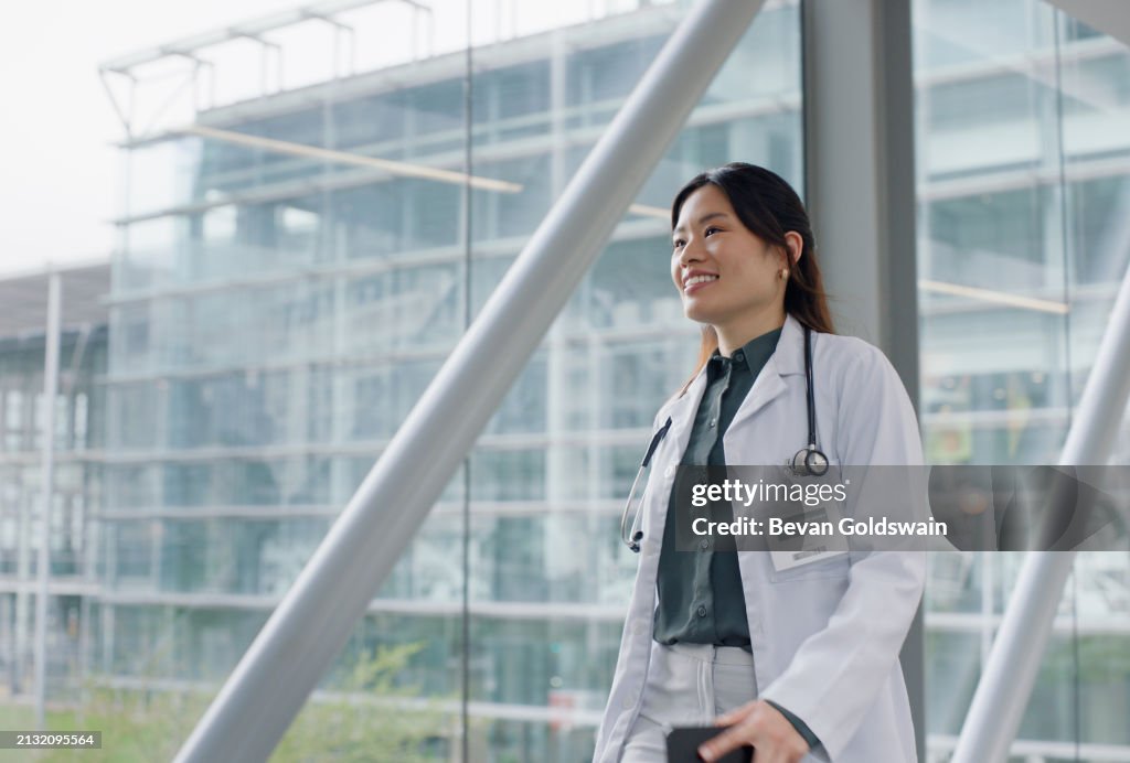 Asiatische Frau, Ärztin und Gang mit Lächeln im Krankenhaus für den öffentlichen Dienst, engagiert und zufrieden. Weibliche Person, Klinik und Lächeln für das Gesundheitswesen mit Termin, Arbeit und Wellness für die medizinische Karriere