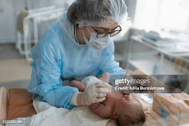 properly equipped female nurse changing diaper and swaddling newborn baby lying on table. - operatiegewaad stockfoto's en -beelden