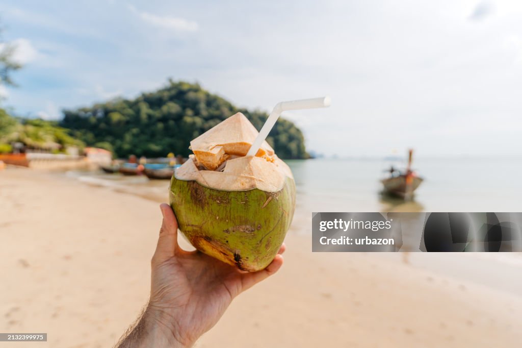 Young Man Holding A Coconut Shell Containing A Drink On The Ao Nang Beach In Thailand