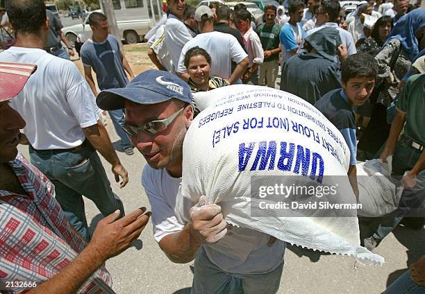 Palestinian youth carries a bag of flour he received from UNRWA staff July 2, 2003 in the West Bank town of Bethlehem. UNRWA, the United Nations...