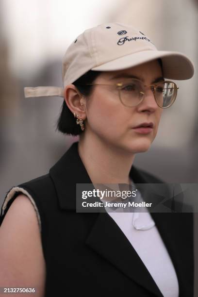 Maria Barteczko seen wearing Ray-Ban gold round retro glasses, gold earrings, Bershka beige baseball cap, WENDYKEI black long sleeveless vest,...