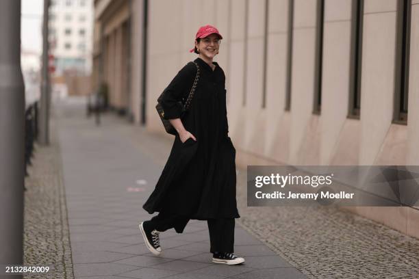 Maria Barteczko seen wearing Ray-Ban gold round retro glasses, Pull&Bear red vintage baseball cap, WENDYKEI black wrinkled oversized midi dress,...