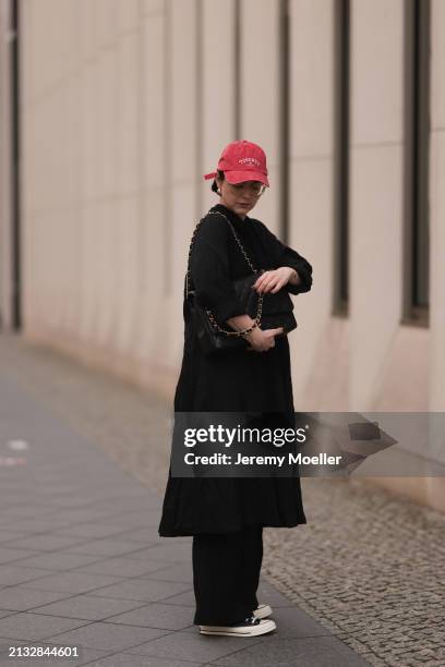 Maria Barteczko seen wearing Ray-Ban gold round retro glasses, Pull&Bear red vintage baseball cap, WENDYKEI black wrinkled oversized midi dress,...