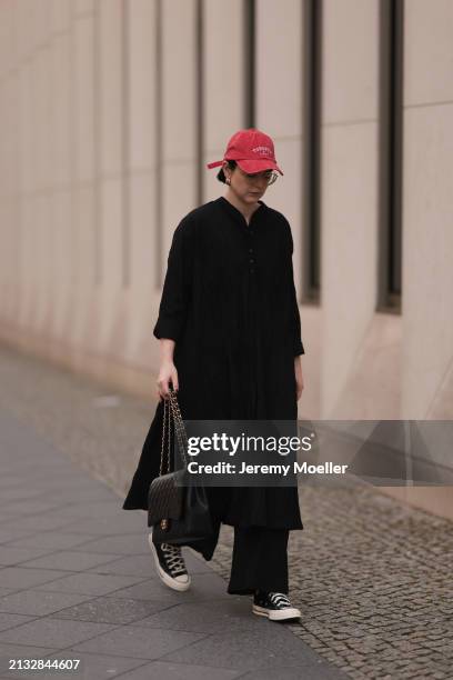 Maria Barteczko seen wearing Ray-Ban gold round retro glasses, Pull&Bear red vintage baseball cap, WENDYKEI black wrinkled oversized midi dress,...