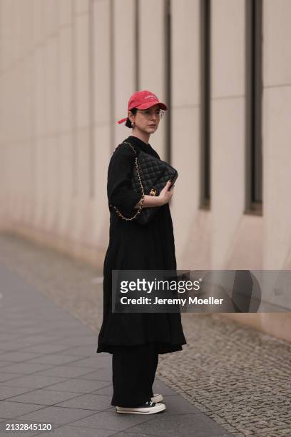 Maria Barteczko seen wearing Ray-Ban gold round retro glasses, Pull&Bear red vintage baseball cap, WENDYKEI black wrinkled oversized midi dress,...