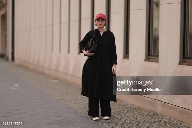 Maria Barteczko seen wearing Ray-Ban gold round retro glasses, Pull&Bear red vintage baseball cap, WENDYKEI black wrinkled oversized midi dress,...