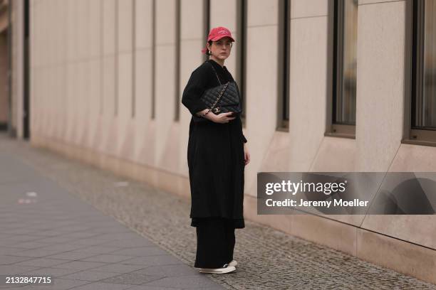 Maria Barteczko seen wearing Ray-Ban gold round retro glasses, Pull&Bear red vintage baseball cap, WENDYKEI black wrinkled oversized midi dress,...