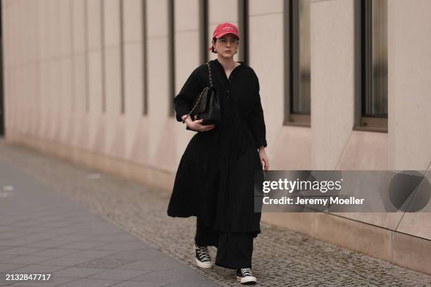 Maria Barteczko seen wearing Ray-Ban gold round retro glasses, Pull&Bear red vintage baseball cap, WENDYKEI black wrinkled oversized midi dress,...