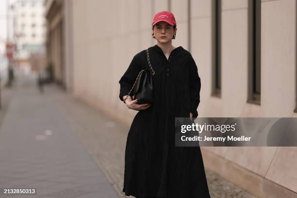 Maria Barteczko seen wearing Ray-Ban gold round retro glasses, Pull&Bear red vintage baseball cap, WENDYKEI black wrinkled oversized midi dress,...