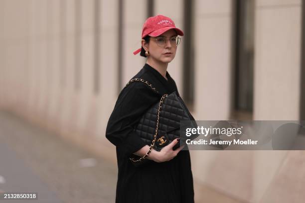 Maria Barteczko seen wearing Ray-Ban gold round retro glasses, Pull&Bear red vintage baseball cap, WENDYKEI black wrinkled oversized midi dress,...