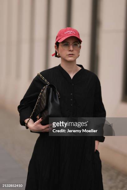 Maria Barteczko seen wearing Ray-Ban gold round retro glasses, Pull&Bear red vintage baseball cap, WENDYKEI black wrinkled oversized midi dress,...