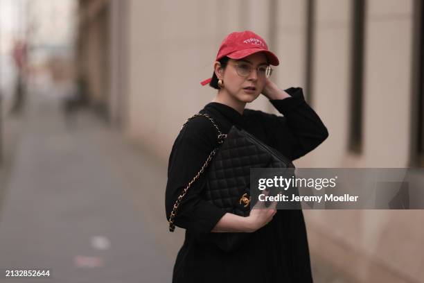 Maria Barteczko seen wearing Ray-Ban gold round retro glasses, Pull&Bear red vintage baseball cap, WENDYKEI black wrinkled oversized midi dress,...