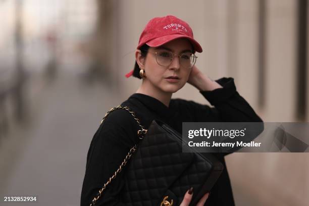 Maria Barteczko seen wearing Ray-Ban gold round retro glasses, Pull&Bear red vintage baseball cap, WENDYKEI black wrinkled oversized midi dress,...