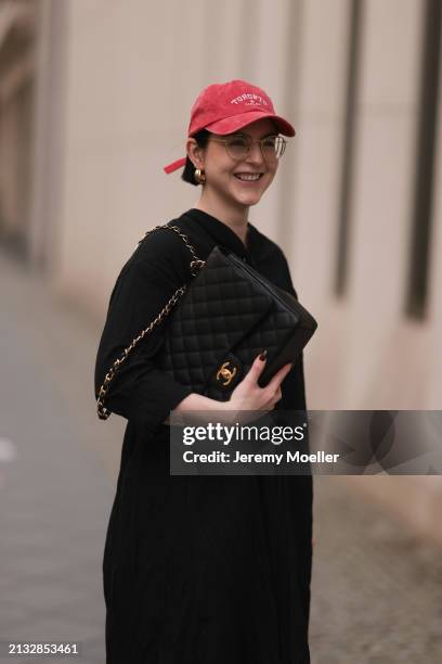 Maria Barteczko seen wearing Ray-Ban gold round retro glasses, Pull&Bear red vintage baseball cap, WENDYKEI black wrinkled oversized midi dress,...