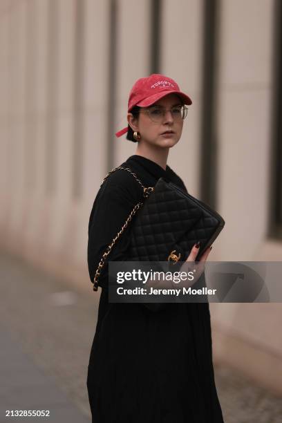 Maria Barteczko seen wearing Ray-Ban gold round retro glasses, Pull&Bear red vintage baseball cap, WENDYKEI black wrinkled oversized midi dress,...